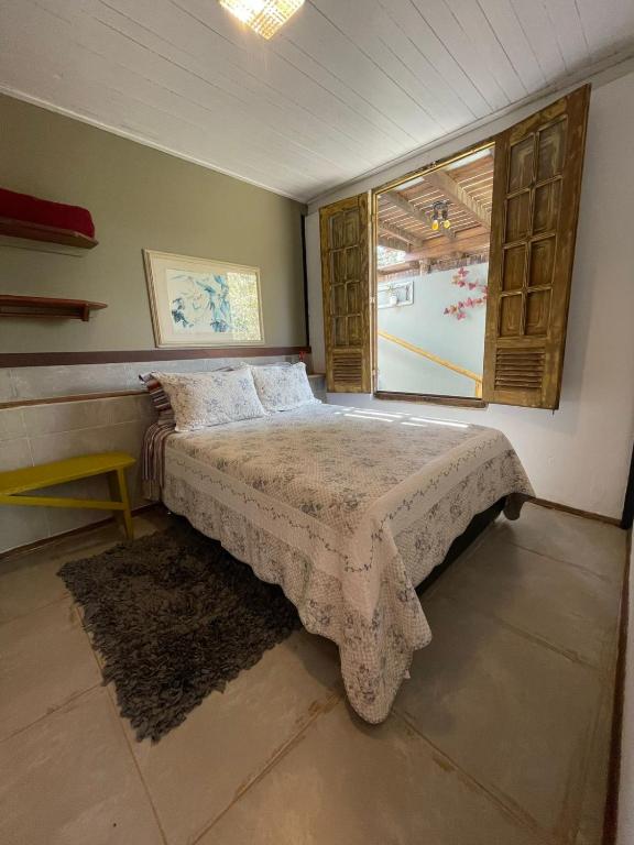 Quarto com colcha floral, janelões de madeira e banco amarelo