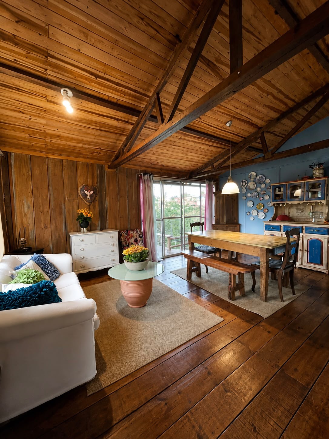 Sala de estar e jantar integradas com sofá branco, mesa de madeira e teto de tábuas aparentes